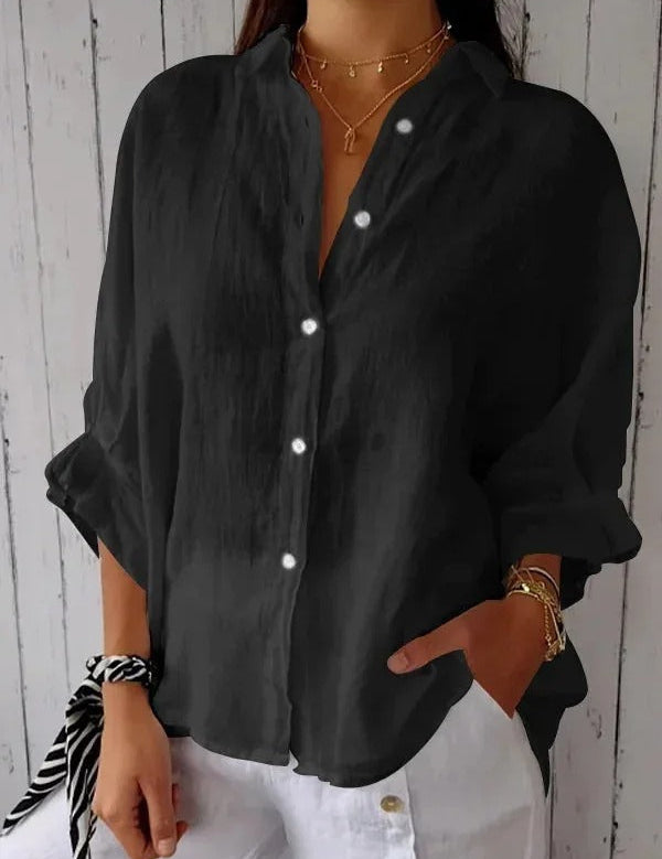 Camicia nera da donna in lino, maniche lunghe, bottoni bianchi, stile casual, abbinata a pantaloni bianchi. Accessori: collane e bracciali dorati.