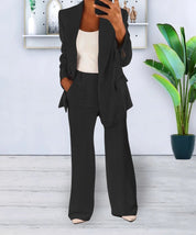 Donna in elegante completo nero, giacca e pantaloni, con top bianco. Sfondo moderno con pianta verde. Moda femminile, abbigliamento formale.