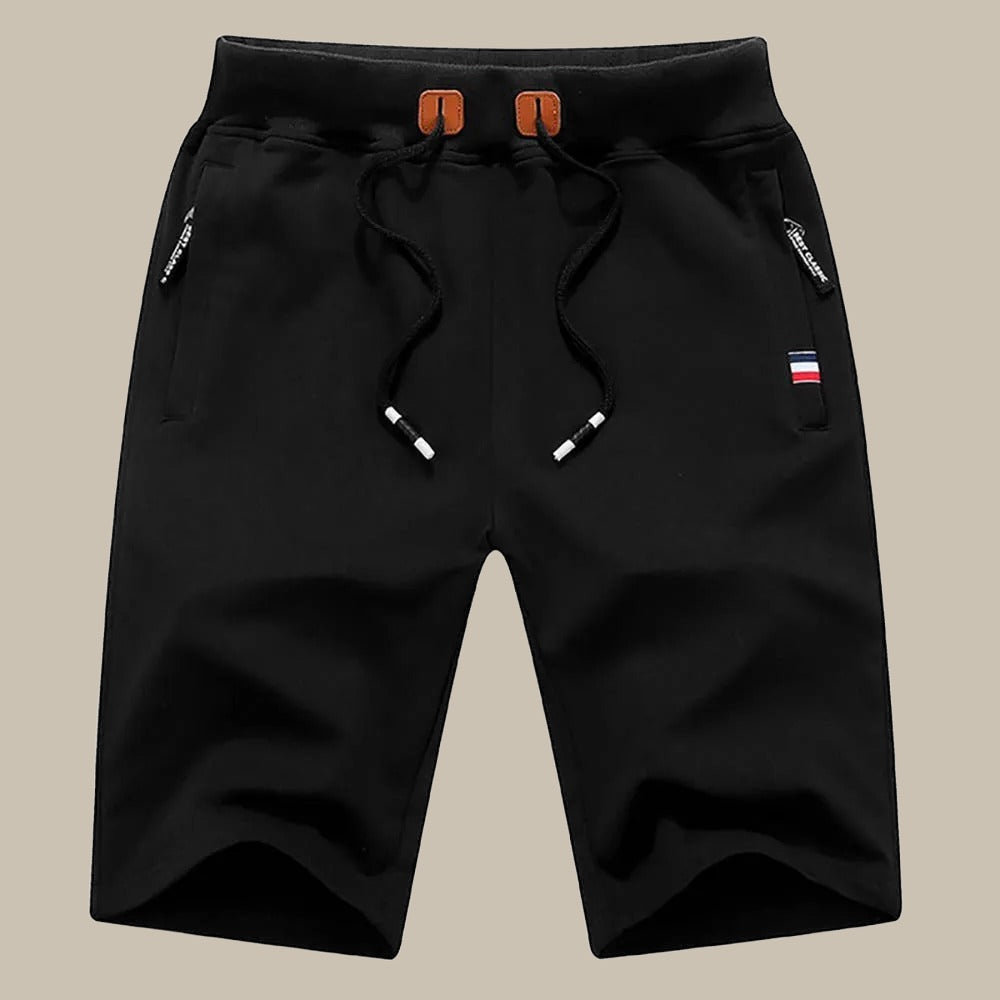 Pantaloncini sportivi neri da uomo con coulisse, tasche con zip e dettaglio bandiera. Ideali per attività sportive e tempo libero.