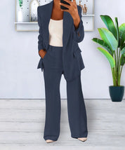 Completo donna elegante blu scuro, giacca e pantaloni a zampa, indossato con top bianco. Sfondo moderno con pianta decorativa.
