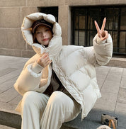 Donna con giacca piumino bianca, cappuccio alzato, seduta su gradino, fa segno di pace. Moda invernale, abbigliamento caldo, stile casual urbano.