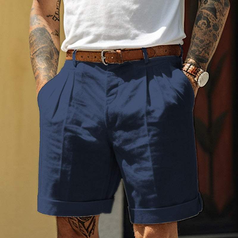 Uomo con pantaloncini blu eleganti, cintura marrone, orologio al polso e tatuaggi sulle braccia. Moda estiva casual maschile.