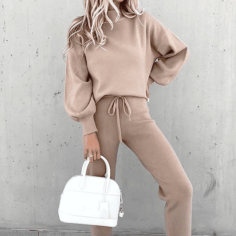 Donna con completo beige, maglione e pantaloni, tiene borsa bianca elegante. Moda autunnale, abbigliamento casual chic, tendenze 2023.