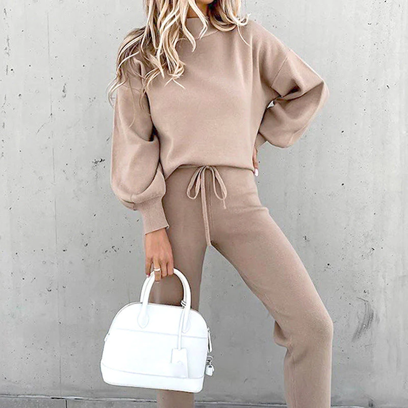 Donna con completo beige in maglia, maglione a maniche lunghe e pantaloni, borsa bianca a mano. Moda autunnale, abbigliamento casual elegante.