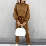 Donna con tuta marrone a maniche lunghe, pantaloni con coulisse, borsa bianca e sneakers. Moda casual autunnale, abbigliamento donna elegante.