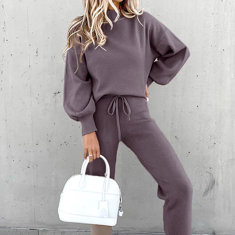 Donna in tuta grigia elegante con borsa bianca, sfondo grigio. Moda autunnale, abbigliamento casual chic, outfit comodo e stiloso.